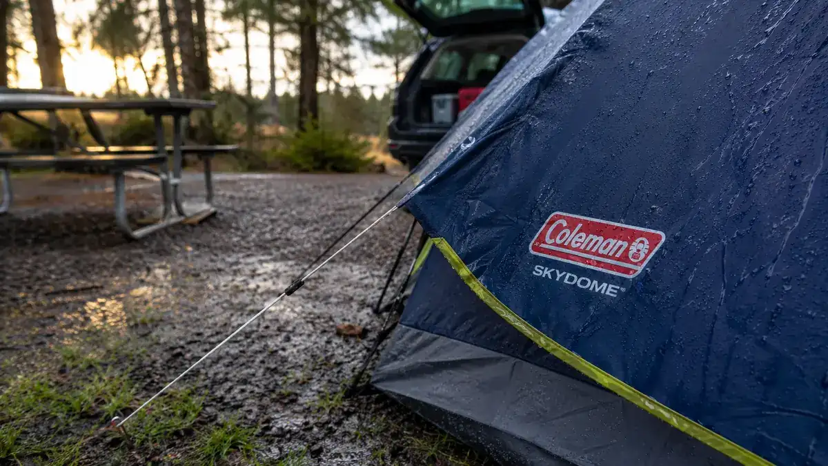 Close-up of the tent's rainfly and guyline staked into wet ground, water beading off the fabric