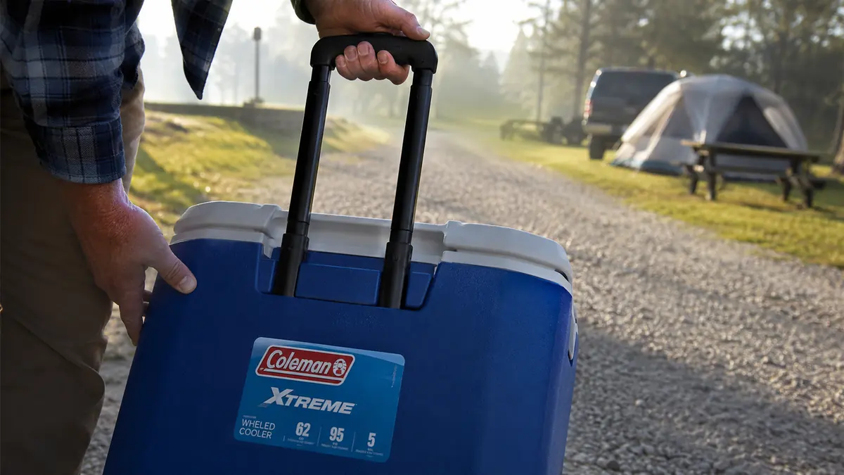 Hand pulling the telescoping handle up on the Coleman Xtreme rolling cooler before wheeling it across a campground road